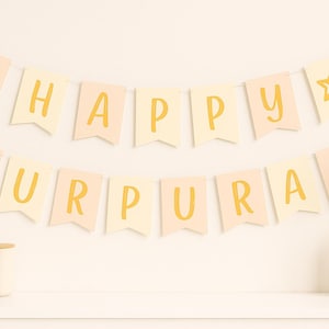 Op de afbeelding: Een slinger met de woorden "HAPPY GURPURAB" in gele letters, gespannen over een witte muur. De slinger heeft een ster en een religieus symbool. Een vaas met een gouden streep en een decoratieve plant staan rechts.
