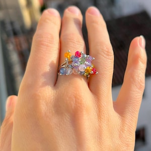 May include: A silver ring adorned with a cluster of colorful beads. The beads are in shades of blue, yellow, pink, and green, creating a vibrant and eye-catching design. The ring is a piece of jewelry.