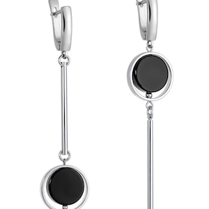 Peut inclure: Boucles d'oreilles pendantes argentées avec une pierre noire circulaire sertie dans un cadre argenté. Une boucle d'oreille a un pendentif en forme de barre verticale, l'autre une barre plus courte. Finition polie, design moderne.