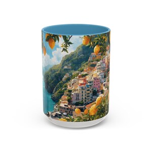 May include: A white ceramic coffee mug with a blue interior and a scenic illustration of a coastal Italian village. The design features colorful buildings, lemons, and a blue sky.