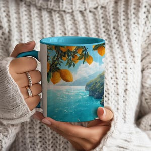 Amalfi Coast mug with blue interior held by person wearing cozy sweater, seaside view artwork visible