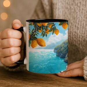 Amalfi Coast mug with blue interior held by person wearing cozy sweater, seaside view artwork visible