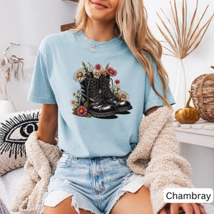 May include: A light blue t-shirt with a graphic of black combat boots with white laces and pink and white flowers.