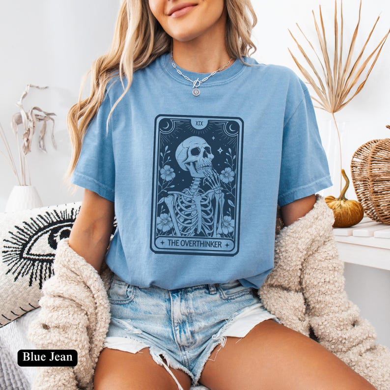 May include: A light blue t-shirt with a graphic of a skeleton holding a flower and the text "The Overthinker".