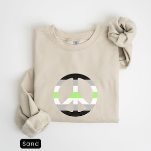 May include: A sand-colored sweatshirt with a peace sign printed on the front. The peace sign is in black, white, and light green, representing the ace flag.