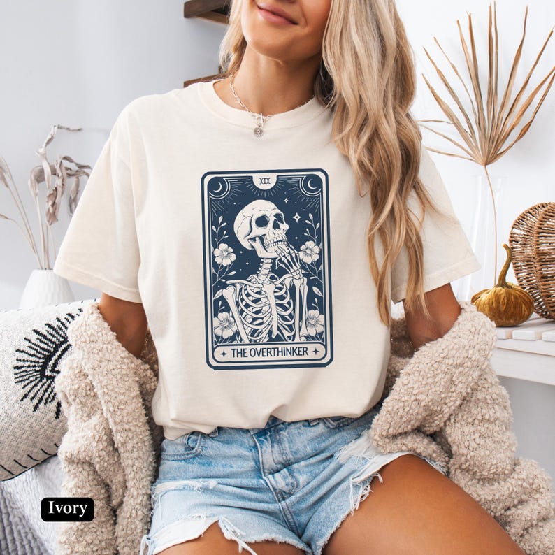 May include: Ivory t-shirt with a graphic of a skeleton with the text "The Overthinker" and a tarot card design.