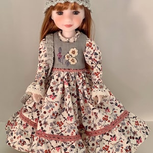 Peut inclure: Une poupée aux cheveux roux portant un chapeau en crochet gris et une robe à imprimé floral. La robe a des manches longues avec des poignets en dentelle, un gilet gris avec broderie florale et une bordure en dentelle rose. C'est un objet de collection.