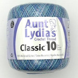 May include: A ball of Aunt Lydia's Classic 10 crochet thread in a variegated blue and purple colorway. The label features the brand name, size 10, and states 100% mercerized cotton. The thread is wrapped in clear plastic packaging for protection.