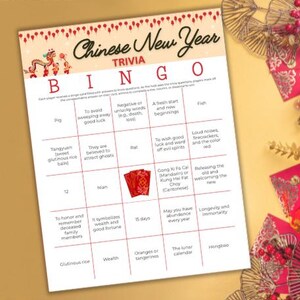 May include: A Chinese New Year Bingo card with a red and white design. The card has a grid of 25 squares with different Chinese New Year traditions and symbols. The squares include words like "pig", "tangyuan", "nian", "wealth", "hongbao", and "the lunar calendar".