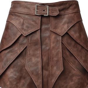 May include: A brown leather skirt with a unique layered design. The skirt features a belt with a silver buckle. The leather has a textured appearance, and the skirt has a distinctive, geometric shape.