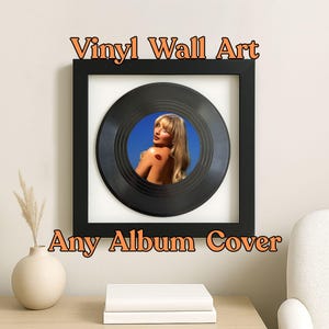 May include: Black framed vinyl wall art featuring an album cover image. The artwork is centered on a white background. The text "Vinyl Wall Art" and "Any Album Cover" are displayed in orange letters.