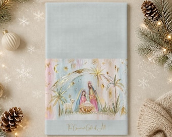 May include: A light blue rectangular tea towel featuring a watercolour illustration of a nativity scene with a star, palm trees, and a lamb. The text "The Greatest Gift of All" is printed in gold script at the bottom of the illustrated section.