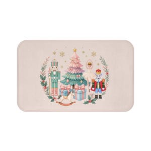 May include: A rectangular bath mat in a light beige color featuring a central illustration of a Christmas tree, a nutcracker, a ballerina, a mouse king, a rocking horse, and gift boxes, all surrounded by a wreath of holly and snowflakes.