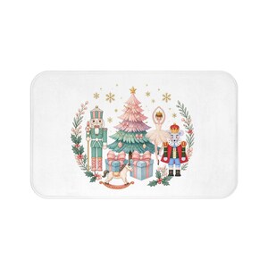 May include: A rectangular bath mat featuring a central illustration of a Christmas tree, a nutcracker, a ballerina, a mouse king, gift boxes, and a rocking horse, all surrounded by a circular wreath of holly and gold snowflakes.