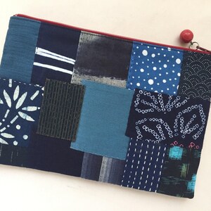 May include: A blue patchwork zippered pouch with a red zipper pull. The pouch is made of different fabrics with various patterns, including white polka dots, white lines, and a white floral design.