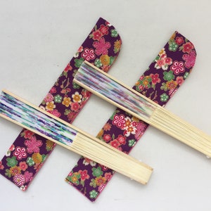 May include: Three folding fans with purple fabric covers featuring a floral pattern. The fans are made of wood and have a white and blue patterned paper insert.