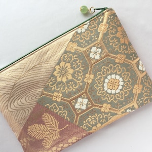 May include: A decorative pouch with a green zipper and a green bead pull. The pouch features a patchwork design with gold, sage green, and burgundy floral patterns. The pouch is made of a textured fabric.