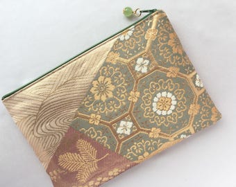 May include: A decorative pouch with a green zipper and a green bead pull. The pouch features a patchwork design with gold, sage green, and burgundy floral patterns. The pouch is made of a textured fabric.