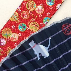 May include: A close-up of two fabric swatches. The top swatch is red with a pattern of gold and white ornaments. The bottom swatch is dark blue with a white striped pattern and a white silhouette of a cat.
