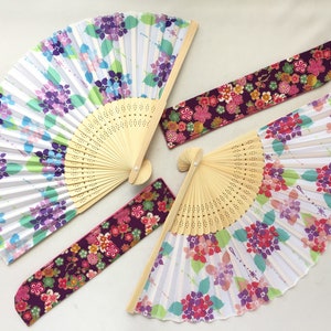 May include: Four folding fans with floral designs. Two fans have a white background with purple and green flowers. One fan has a purple background with pink and red flowers. The last fan has a purple background with pink, red, and white flowers.