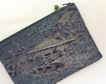 May include: A dark blue zippered pouch with a green zipper pull and a green bead. The pouch has a geometric pattern in shades of brown, green, and white.