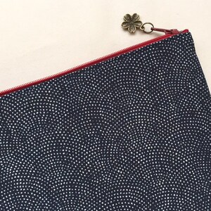 May include: A navy blue zippered pouch with a white polka dot pattern. The pouch has a red zipper and a decorative flower charm.