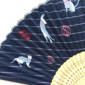 May include: A blue and white folding fan with a striped pattern and a white cat design. The fan has a wooden handle with a decorative pattern.