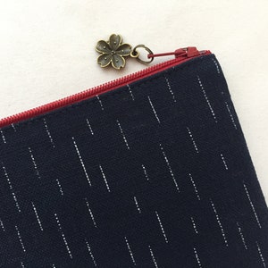 May include: A dark blue zippered pouch with a white stripe pattern. The zipper pull is a small bronze flower charm.