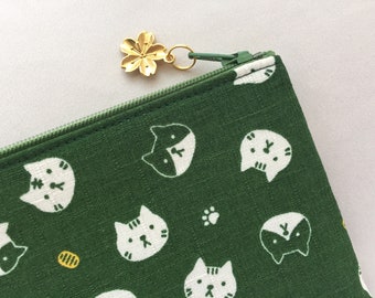 May include: A green zippered pouch with a gold flower charm. The pouch is decorated with a repeating pattern of white cats.