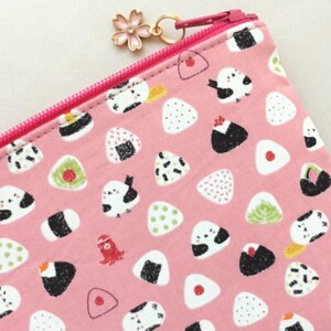 May include: A pink zippered pouch with a white and black onigiri (Japanese rice ball) pattern. The pouch has a pink zipper and a gold charm with a pink flower.