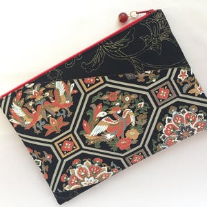 May include: Black clutch with a red zipper and a gold bead zipper pull. The fabric features a geometric pattern with birds, flowers, and foliage in red, gold, and cream colors.