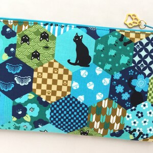 May include: A blue and green zippered pouch with a hexagonal pattern featuring black cats, flowers, and geometric designs. The pouch has a gold zipper pull.