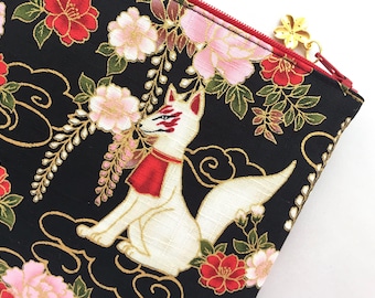May include: A black zippered pouch with a white fox and floral pattern. The pouch has a gold zipper pull with a flower charm.