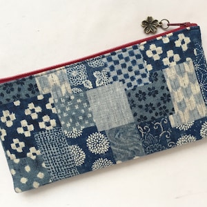 May include: A blue and white patchwork zippered pouch with a red zipper and a small metal charm. The pouch is made of fabric with a variety of traditional Japanese patterns.