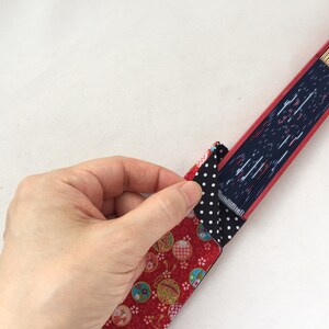 May include: A red and black fabric fan with a white polka dot pattern. The fan is folded and being held by a hand.