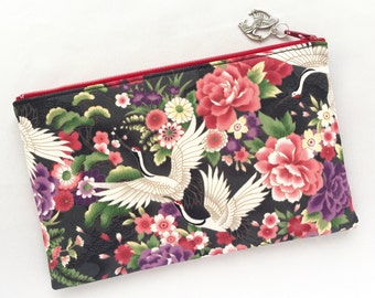 May include: A black zippered pouch with a red zipper pull. The pouch is decorated with a floral pattern featuring pink, red, and white flowers, green leaves, and white cranes.