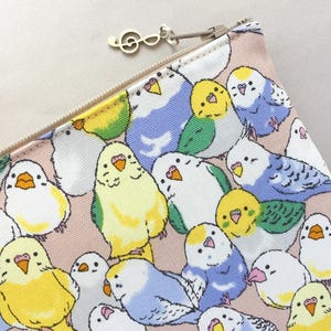 May include: A zippered pouch featuring a repeating pattern of colorful parakeets in shades of yellow, blue, green, and white on a pink background. A silver treble clef charm hangs from the zipper pull.