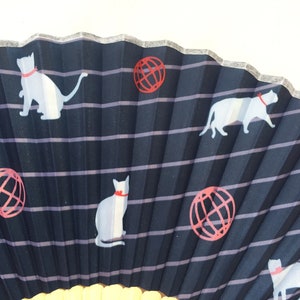 May include: A black folding fan with a white and red design. The fan features a repeating pattern of white cats and red globes.