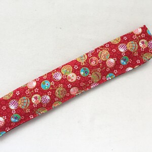 May include: A red fabric chopstick case with a pattern of colorful ornaments and white flowers.