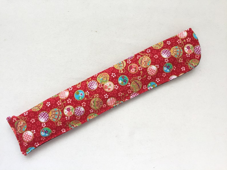 May include: A red fabric chopstick case with a pattern of colorful ornaments and white flowers.