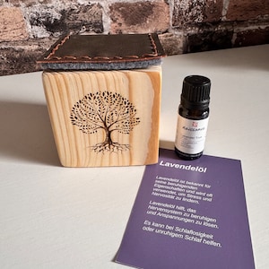 Könnte beinhalten: Eine Holzkiste mit einem Baumdesign und eine kleine Flasche mit Lavendel-Ätherischem Öl. Die Flasche ist mit "Lavender True" und "naissance" beschriftet. Der Text auf der Karte lautet: "Lavendelöl ist bekannt für seine beruhigenden Eigenschaften und wird oft verwendet, um Stress und Nervosität zu lindern. Lavendelöl hilft, das Nervensystem zu beruhigen und Verspannungen zu lösen. Es kann bei Schlaflosigkeit oder unruhigem Schlaf helfen."