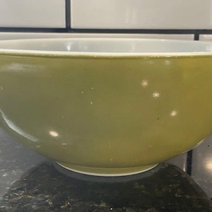 May include: A vintage olive green mixing bowl with a white interior. The bowl has a rounded shape with a flared rim and two small handles. This kitchenware item is ideal for mixing ingredients.