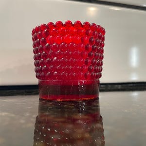 May include: A red glass candle holder with a textured, bubble-like surface. The holder is round and has a wide opening at the top.
