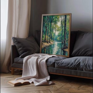 May include: A framed painting of a forest scene with a river flowing through it. The painting is in a wooden frame and is hanging on a wall above a gray couch.
