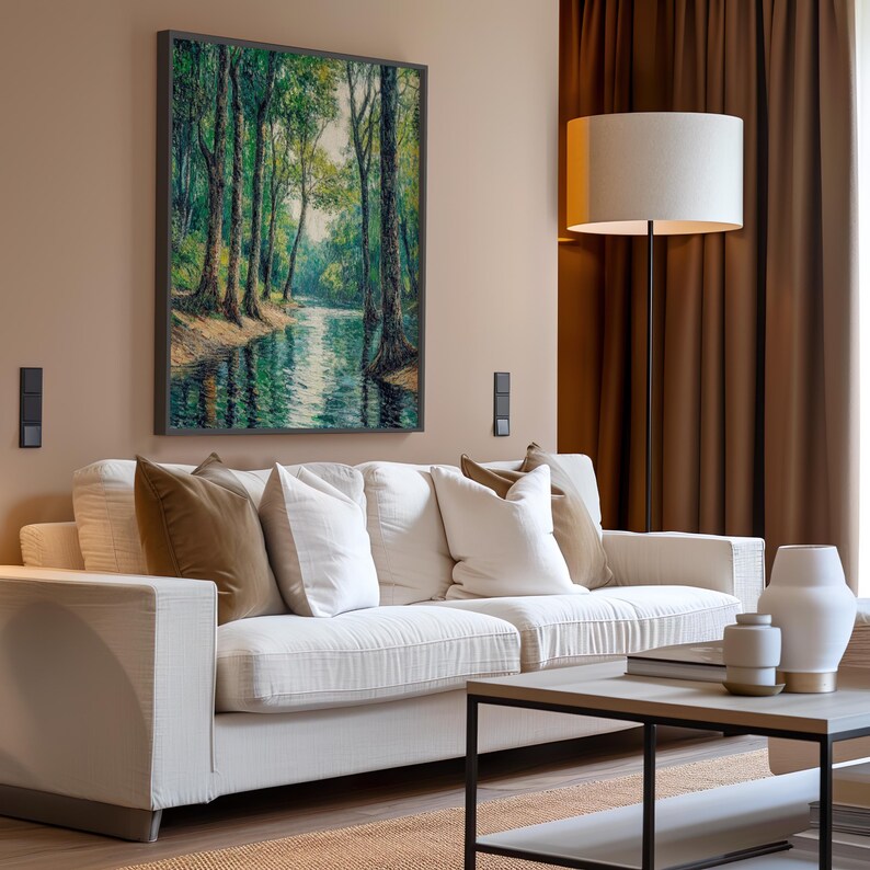 May include: A white sofa with brown and white pillows sits in a living room with a painting of a forest scene above it. A floor lamp with a white shade stands next to the sofa. A coffee table with a book and decorative objects sits in front of the sofa.