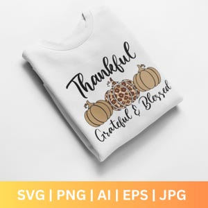 Puede incluir: Sudadera blanca con la frase "Thankful, Grateful & Blessed" y tres ilustraciones de calabazas. La calabaza central tiene un diseño de estampado de leopardo. El diseño es de temática otoñal.