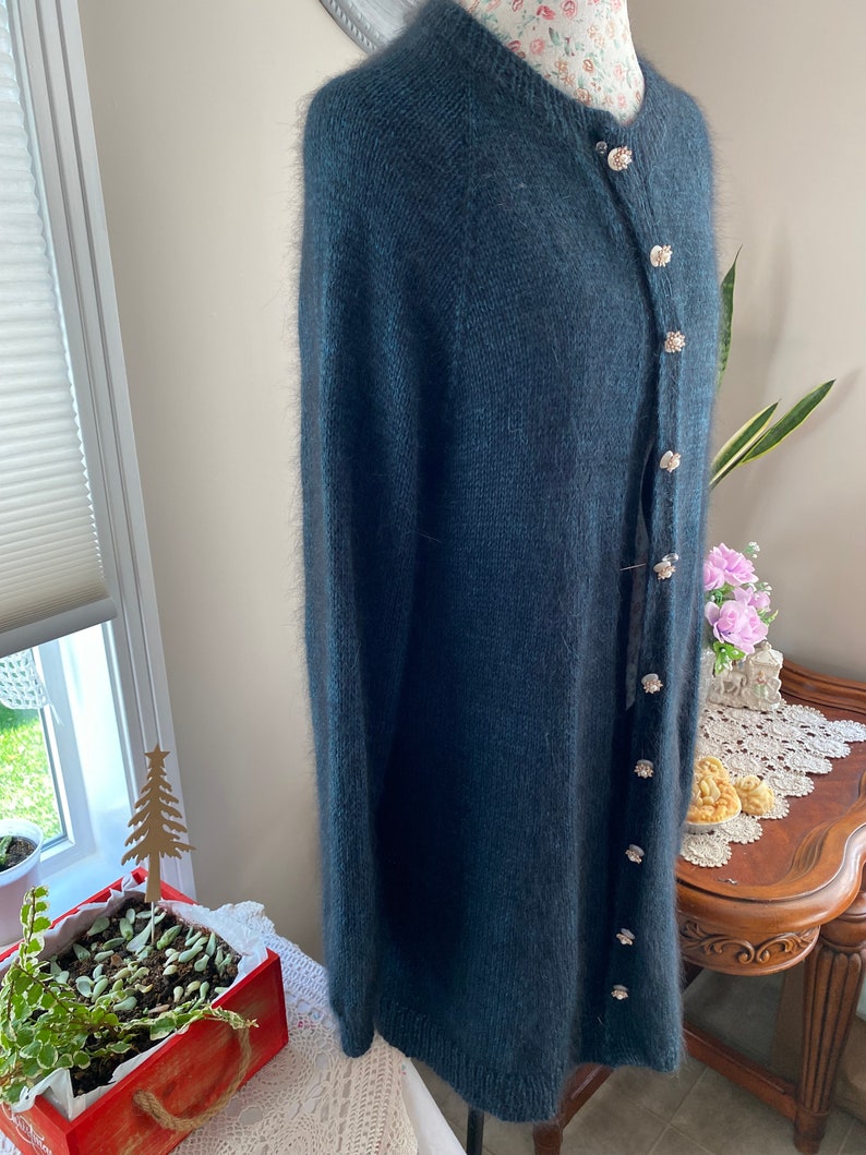 May include: A dark blue fuzzy cardigan with a button closure. The cardigan has a round neckline and long sleeves.
