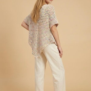 May include: A short-sleeved, open-weave crochet top in pastel colors paired with off-white linen pants. The top has a loose fit and a slightly asymmetrical hem. The pants are wide-legged and casual, creating a relaxed, summery look.