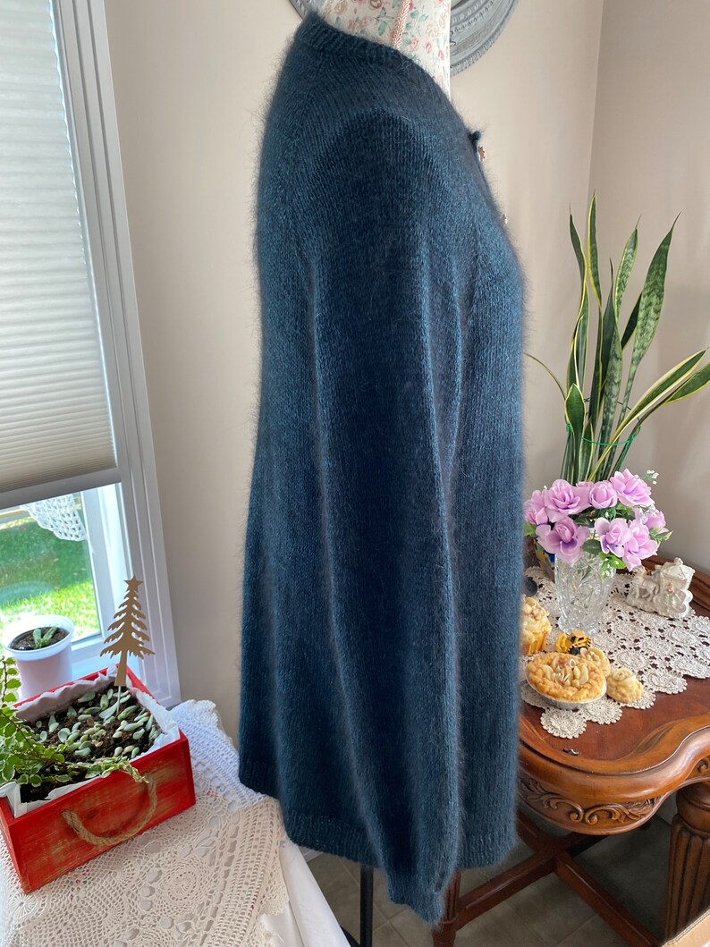 May include: A long-sleeved, dark blue cardigan sweater with a fuzzy texture. The sweater has a button closure and a ribbed hem.