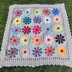 Puede incluir: Una manta de ganchillo gris con un borde festoneado. La manta est&aacute; hecha de cuadrados con dise&ntilde;os de flores de colores en tonos de rojo, amarillo, azul, verde y rosa.